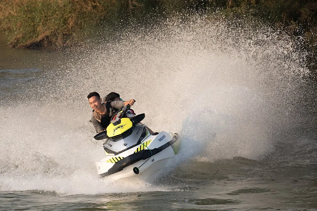 1024px Couple of teenagers riding a personal watercraft splashing on the Mekong in Laos