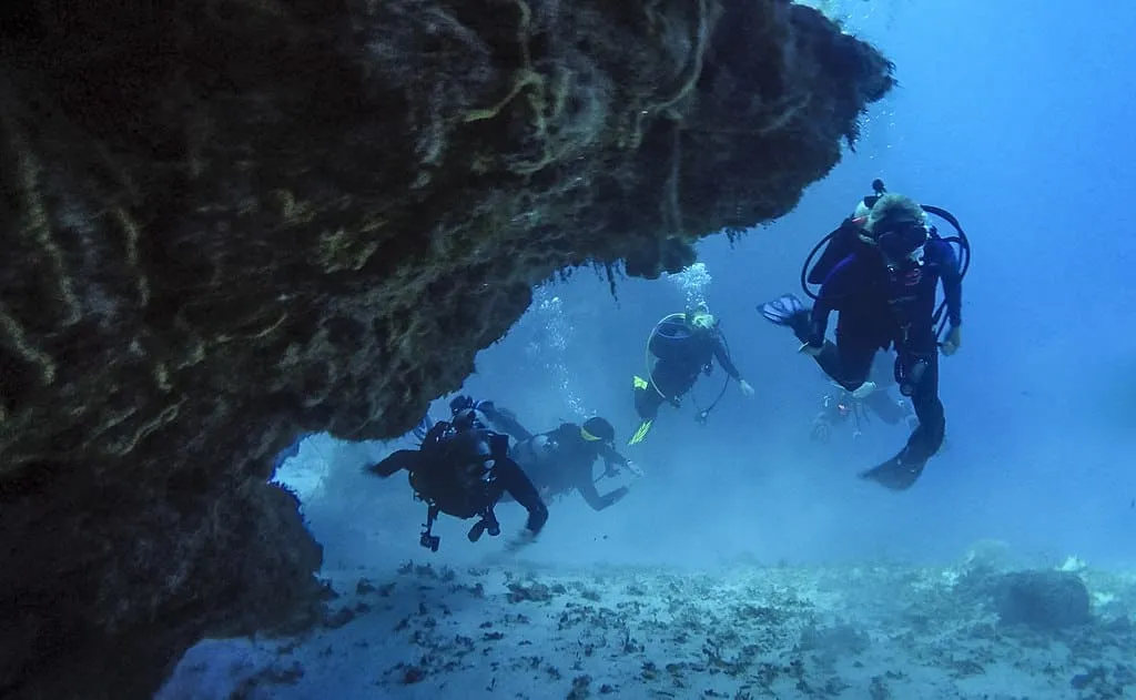 1024px Scuba Divers in Cozumel Mexico swimming through a coral cave 2
